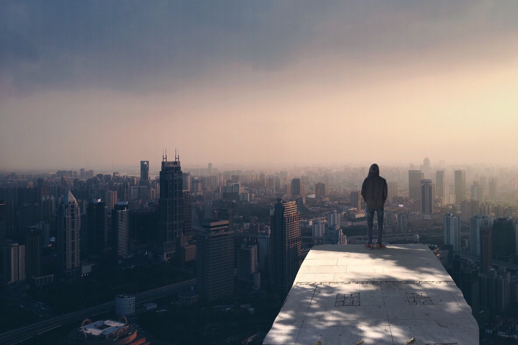 a boy standing on the highest building of the city. he is looking the whole city. he wear coat and jeans.