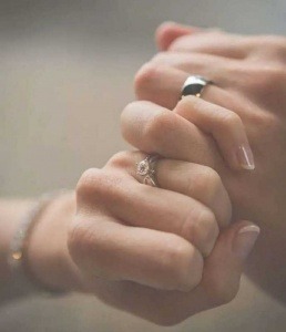background is blur. boy hold her hand with his hand's finger. both have rings in their finger. girl also have a bracelet in her hand which is blur.